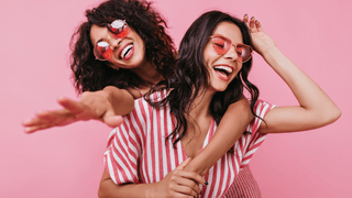 Two friends laughing in front of a pink background