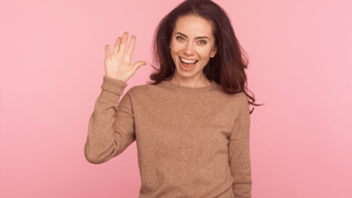Woman waving in front of pink wall