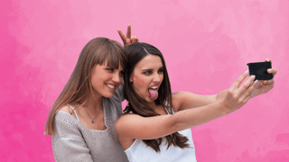 Two friends taking a selfie in front of a pink backdrop