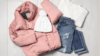 A flat lay image of a pink coat, cozy white hat, white sweater, and jeans
