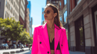 Woman wearing a hot pink blazer jacket over a black crop top paired with layered jewelry